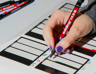 Photograph of a hand colouring in a pixel, holding an Edding pen