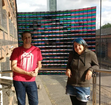 Photograph of Matt Parker and Katie Steckles standing near a section of MegaPixel image in the window at the Science and Industry Museum.