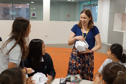 A photo of Think Maths presenter Zoe holding a paper dodecahedron, talking to a group of school students
