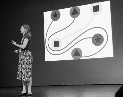 A black-and-white photo of Zoe talking in front of a projector screen